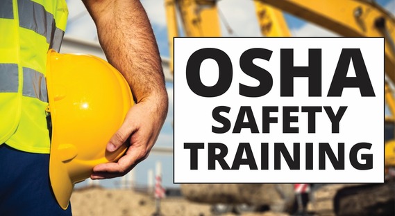 An "OSHA Safety Training" sign in front of some excavators and beside a man in a reflective vest holding a hard hat.