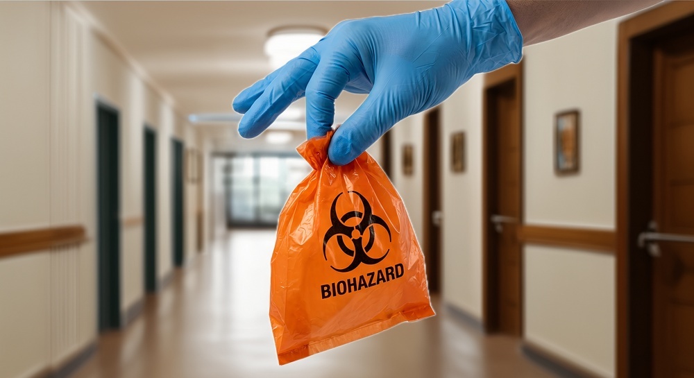 A latex-glove-wearing hand holds an orange biohazard bag.