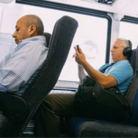 Two bus passengers sitting, looking at their phone