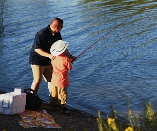 dad showing son in cowboy hat how to fish