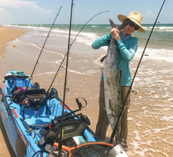 woman next to kayak in surf, holding silver fish