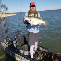 Blake standing in his kayak holding a large bass