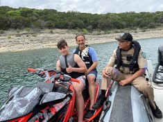 Game Warden on a boat checking a jet ski operator for safety equipment.
