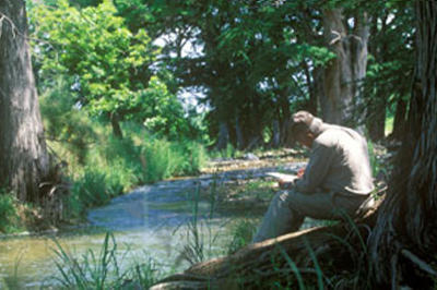 Image of a man sitting next to a small river.