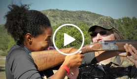 girl holding rifle with instructor, video link