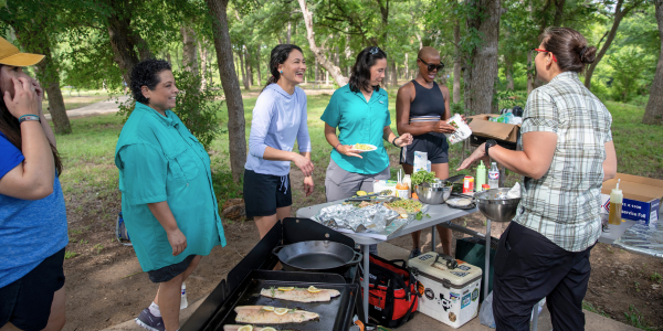 Image of a group of women around a grill, cooking fish.