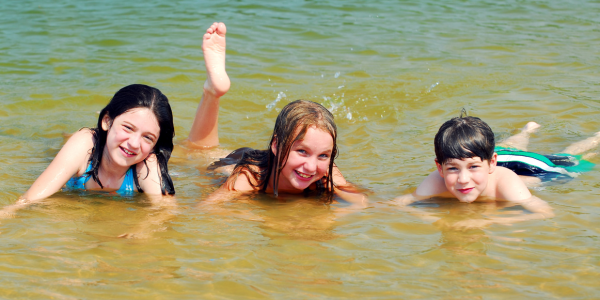Three kids laying in shallow water in a lake.