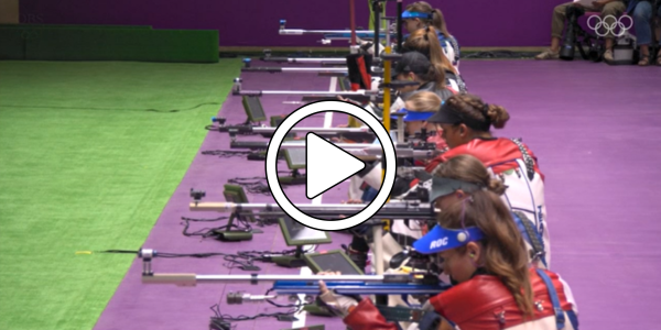A line of athletes at the Olympics aiming rifles.