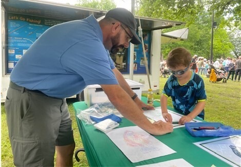 Picture of a volunteer assisting a youth create a fish rubbing