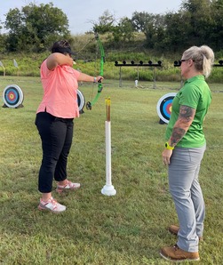 Female instructor monitors archery as a student draws a bow
