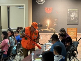 Hunter Ed instructor helping student in class with an inert firearm