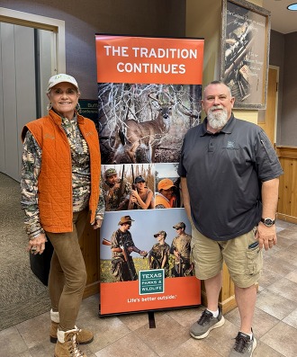Male and Female hunter education teachers pose on either side of an educational banner