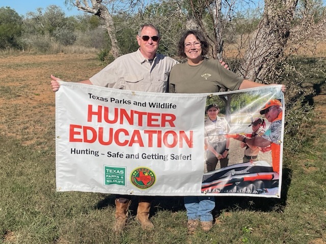 Ranch owners holding up Hunter Ed banner on their property