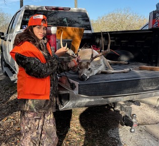 Girl poses with deer harvest on the back of a truck