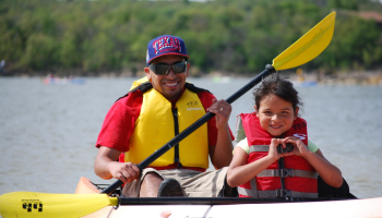 girl in kayak with dad making heart symbol with her hands