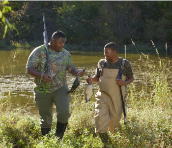Two men holding duck harvest in field, link