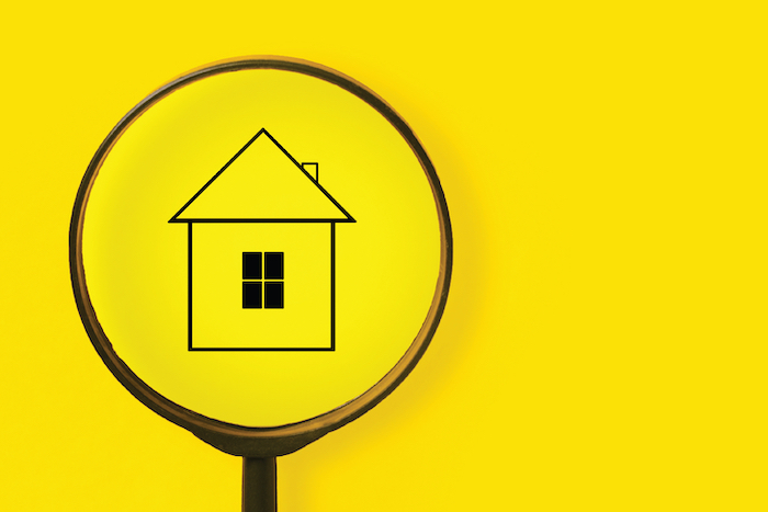 A yellow background with a black magnifying glass over a simple line-drawing of a house