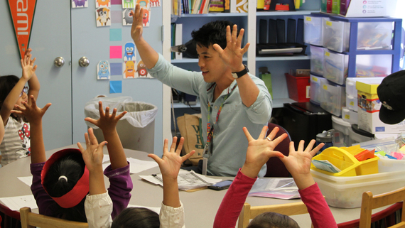 teacher in classroom, hands raised