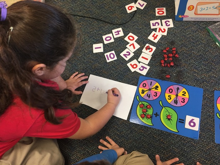 Young student writing numbers on paper, on carpeted floor of math classroom