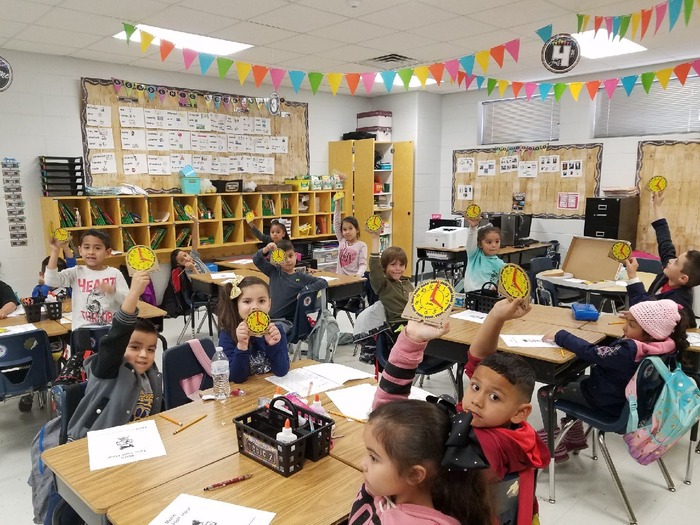 Students in class holding clocks.