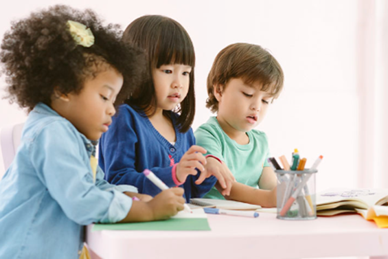 Children at a table writing with markers