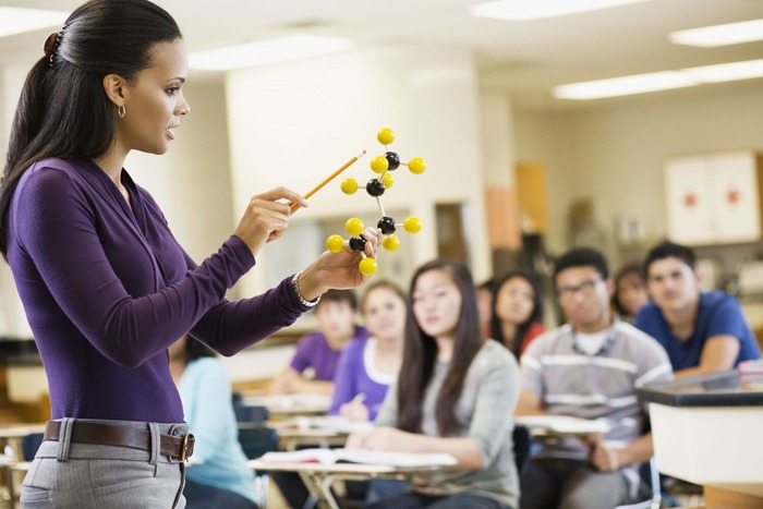 HS Chemistry teacher and students in classroom looking at model of an element.