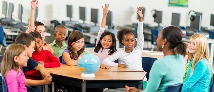 teacher at a table with students holding their hands up