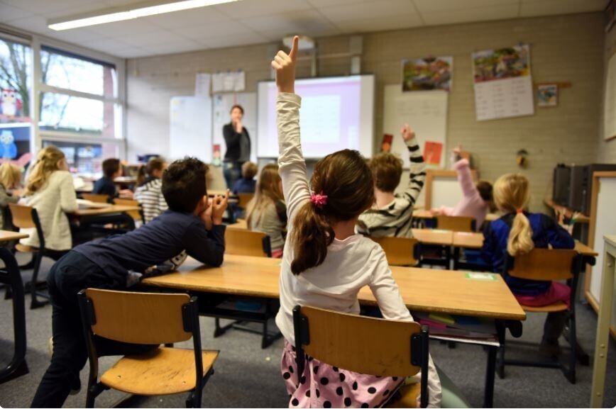 clasroom seen from behind, girl with hand raised