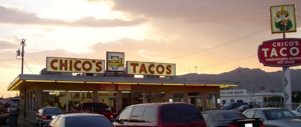 Mexican restaurant with big lit-up signs reading ?Chico?s Tacos? and a full parking lot