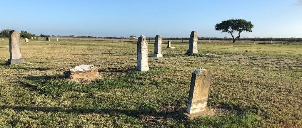 Historical marker with Historic Texas Cemetery medallion in a flat cemetery with widely spaced headstones