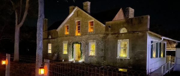 Historic stone home at night, with warm golden light spilling out the windows