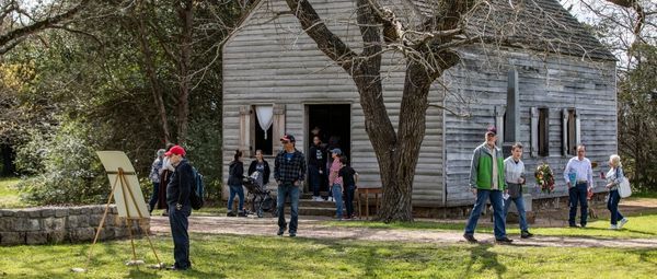 Museum visitors at a small wooden building in spring