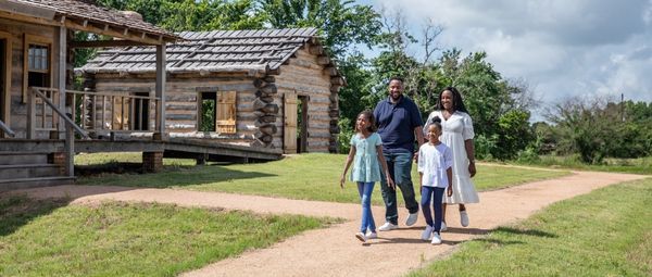 Family of four walking down a path past log buildings