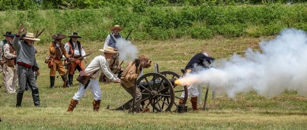 Historical reenactors fire a cannon in a grassy field