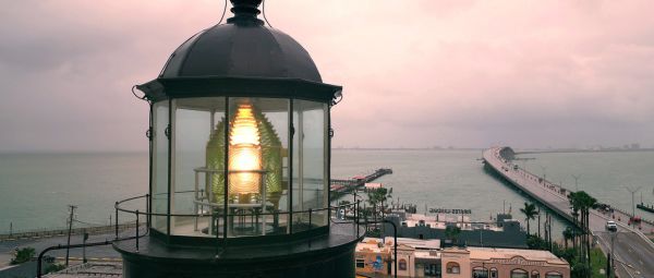Closeup of the lamp in a historic lighthouse at dusk, with a causeway and barrier island in view in the distance