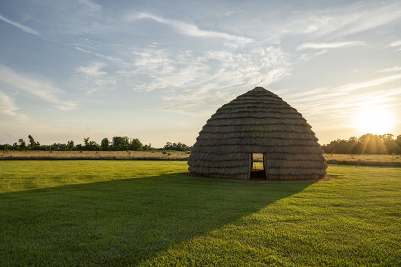 Native American grass house with sun setting behind