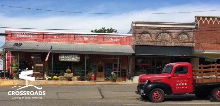 Photo of a small town with a truck passing through. In the corner it says Crossroads.