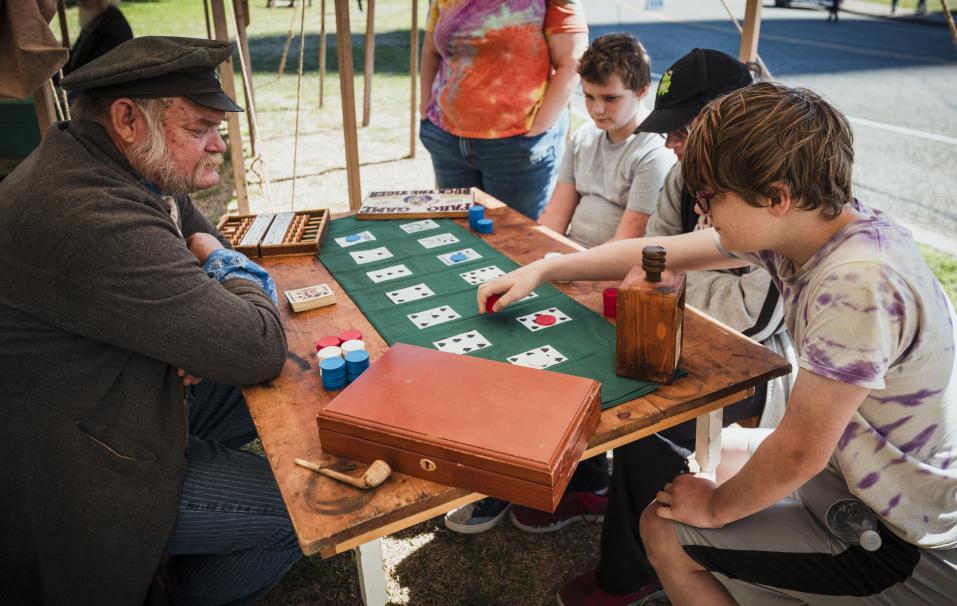 A man dressed in frontier clothing playing a card game with young children