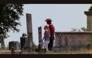 Color image of tall man wearing a cowboy hat and a young woman walking through a historic cemetery