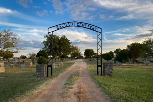 Photograph of a cemetery entrance with a wrought iron arch with the text that reads "Bagdad Cemetery"