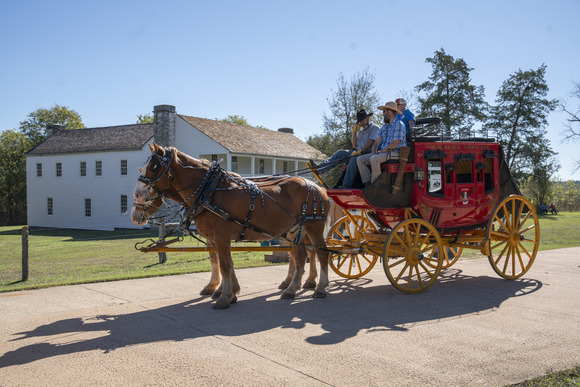 Red stagecoach led by horses in front of a white wooden building