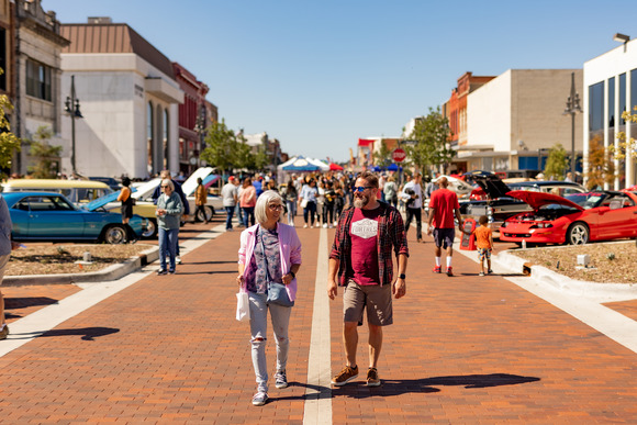 Man and woman walk down main street with classic cars in the background 