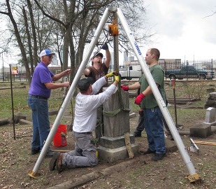 A group of people prepare to lift a gravestone with a tripod