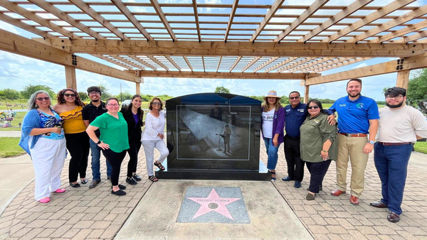 Color photograph of a crowd posing outside next to the headstone memorial for Mexican American country artist Freddy Fender