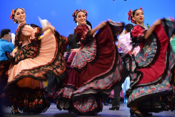 Three female ballet folklorico dancers on a stage in colorful dresses 