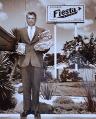 Man in suit holding merchandise stands in front of billboard sign