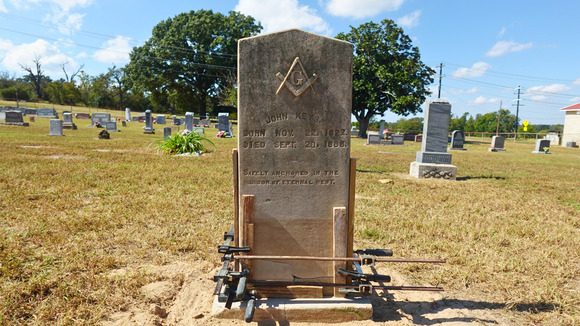 Color photo of a cracked concrete headstone in a historic cemetery undergoing a repair using clamps and mortar