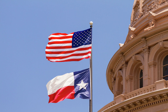 United States and Texas flags flying together by the Capitol building
