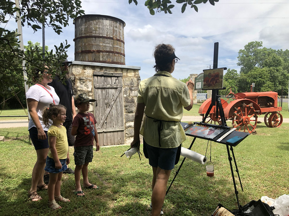 Woman paints tractors while a family of four watches 