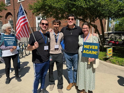 Four men and a woman holding a never again sign and a U.S. flag are pictured smiling on a college campus. 